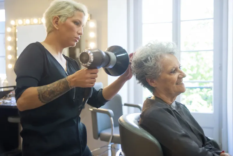A skilled hair stylist blow drying a senior woman's hair in a modern salon